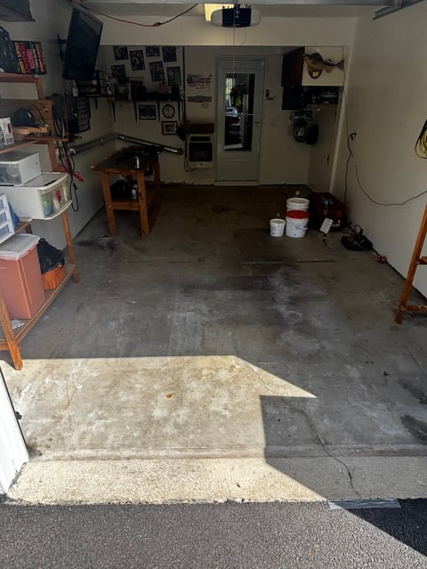 Interior of a garage with concrete floor, wooden workbench, tool cabinets, and various equipment on walls