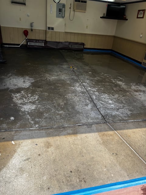 Empty gymnasium floor under renovation showing concrete surface with blue trim and utility equipment on walls